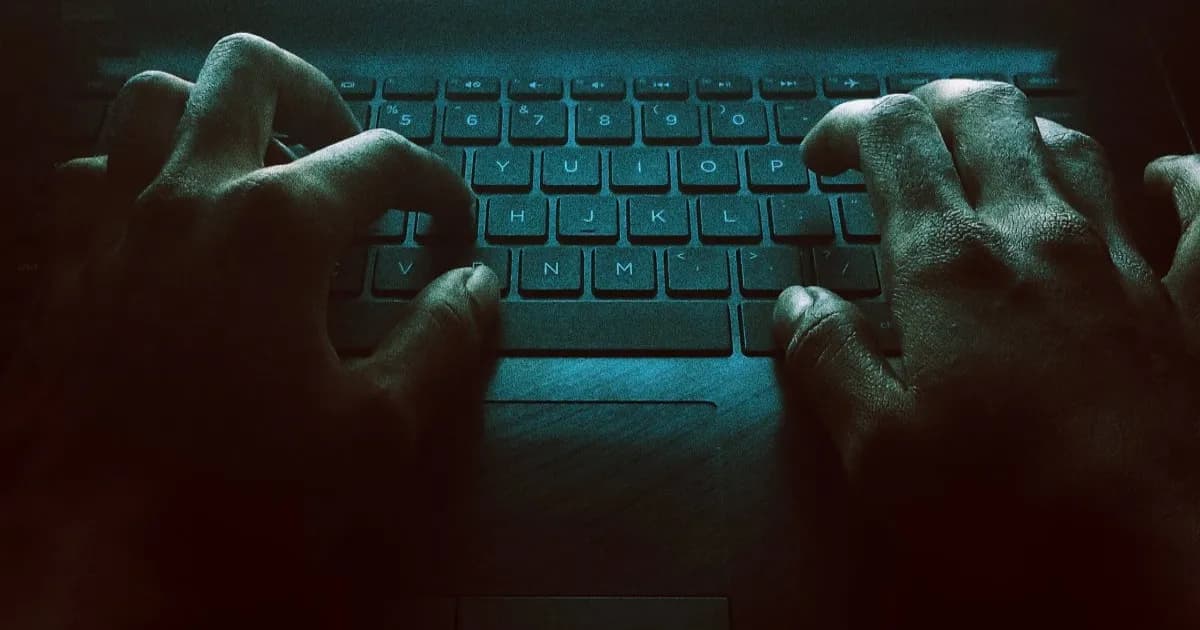 Tangan seorang pria mengoperasikan keyboard dalam gelap, menggambarkan serangan siber terhadap peramban AI.